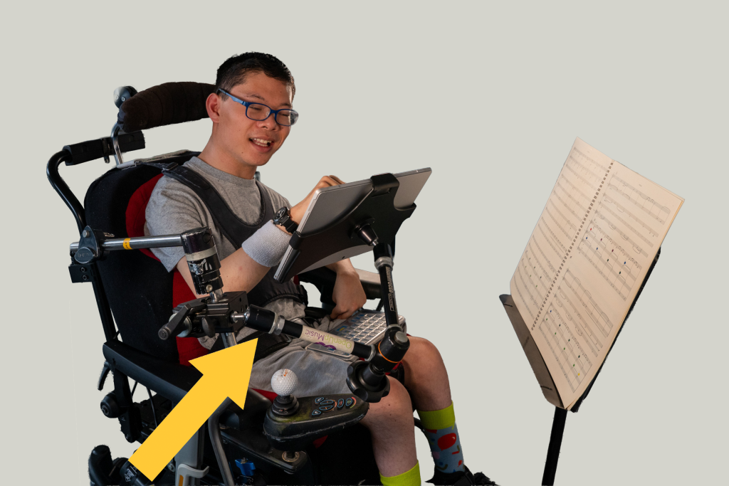 A young musician plays the Clarion. His tablet is attached to his wheelchair and held by the Manfrotto Variable Friction Arm (VFA). A yellow arrow points to the VFA.