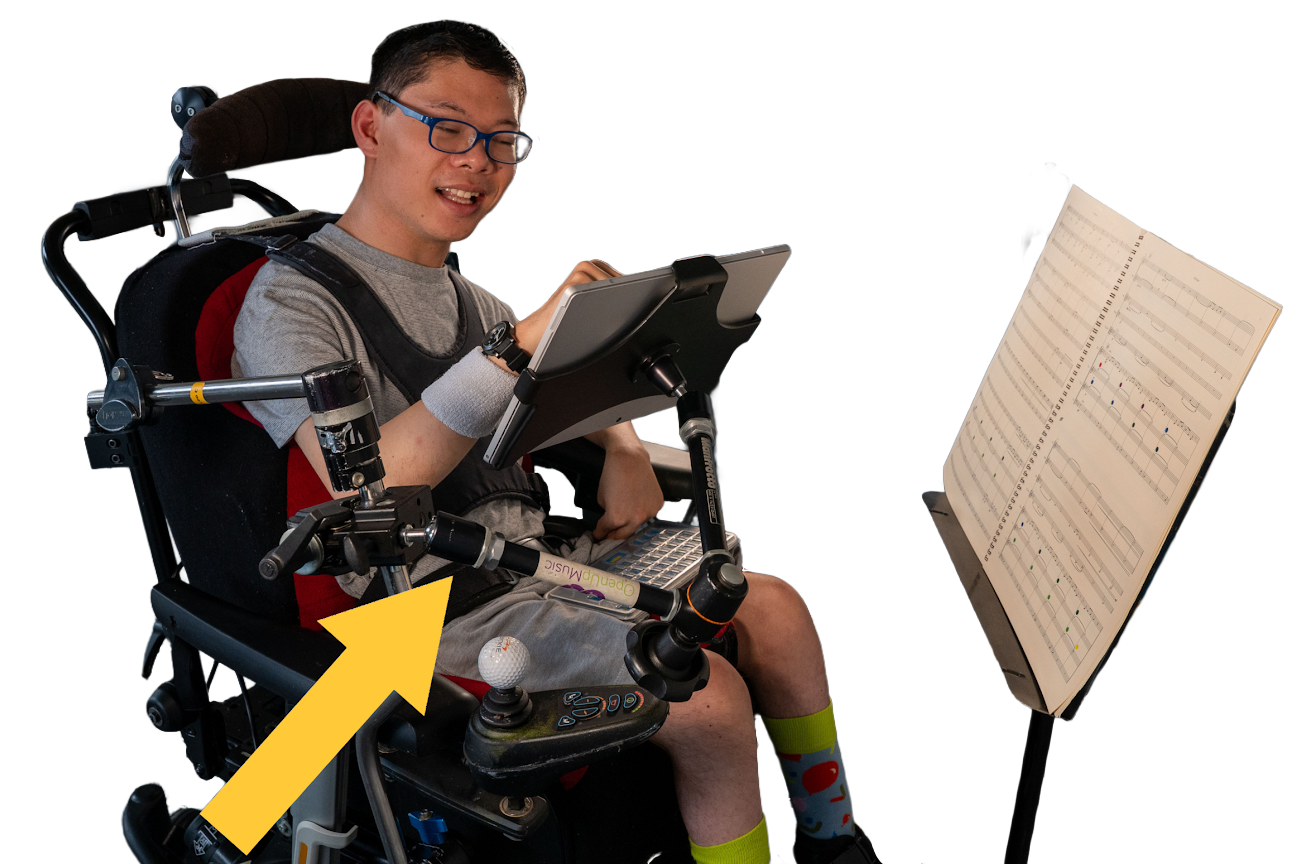 Musician in a wheelchair playing the Clarion using his finger on an iPad, with his music on a music stand in front of him. An arrow points to the adjustable arm used to hold the Clarion.