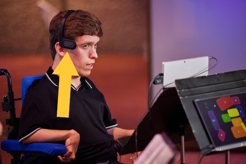 A young musicians plays the Clarion using the Quha Zono head mouse. A yellow arrow points to the Quha Zono on his head.