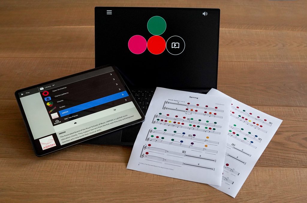 Picture showing the app on iPad, a pattern on a Windows device and a printed score of "Spiring". The score has coloured dots showing Clarion notation.